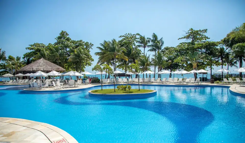 Piscina com ilha e palmeiras de frente para o mar em resort pé na areia no Guarujá